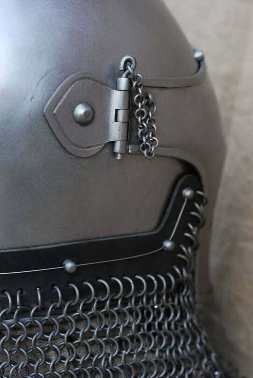 Close-up of a metallic helmet with chain details on a neutral background