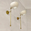 Two wall-mounted lamps with gold arms and white spherical lights on a light gray wall.