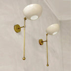 Two wall-mounted lamps with gold arms and white spherical lights on a light gray wall.