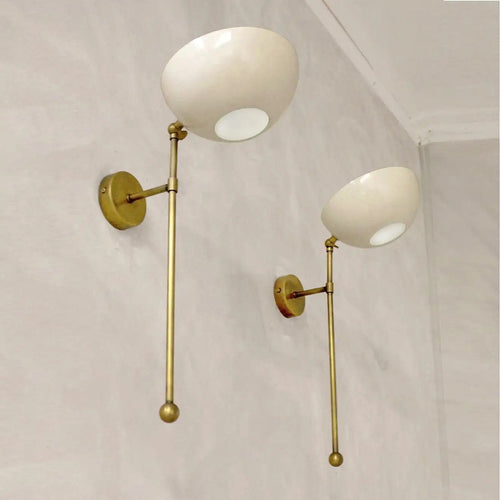 Two wall-mounted lamps with gold arms and white spherical lights on a light gray wall.