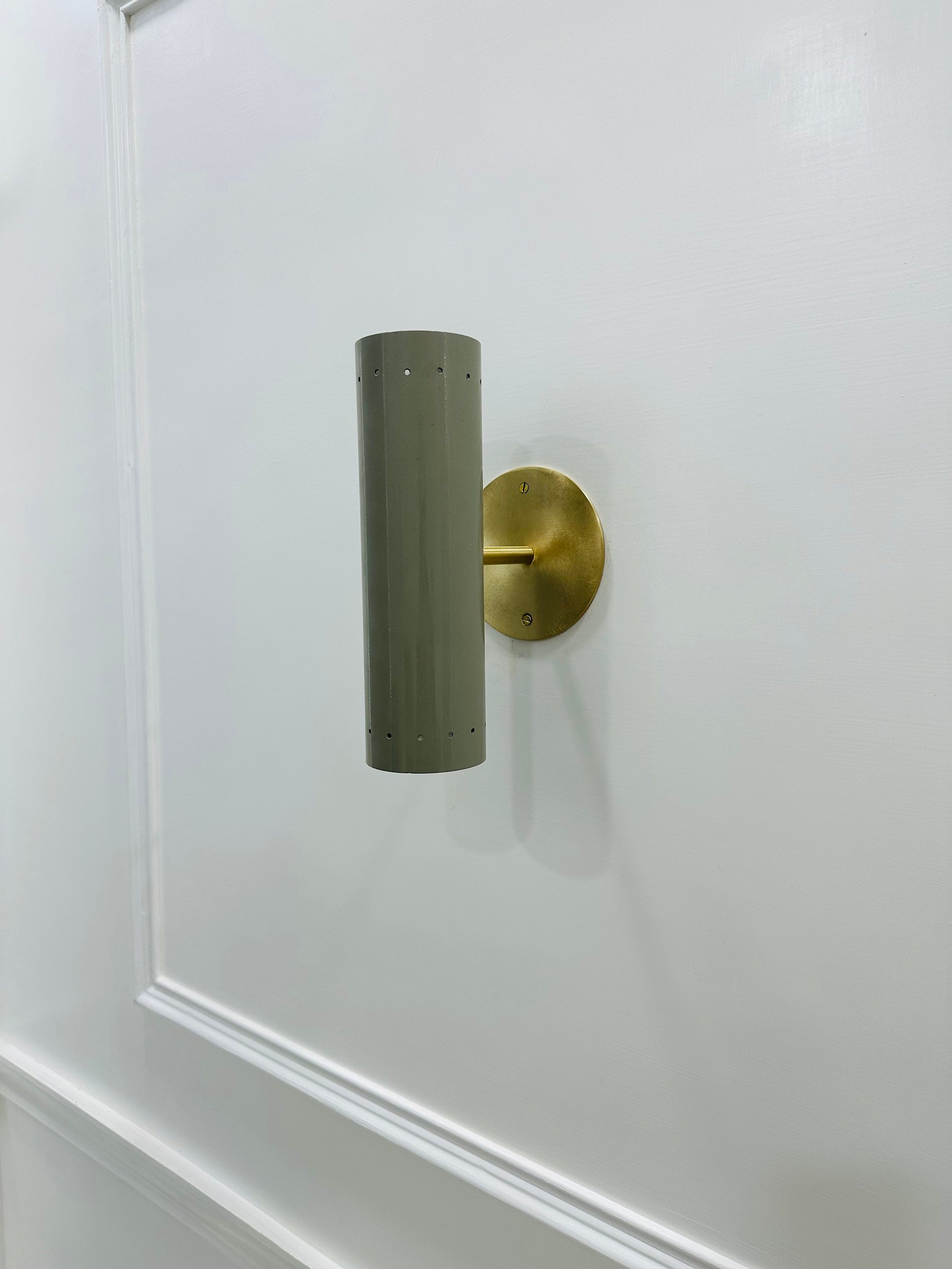 Wall-mounted cylindrical light fixture with a brass fitting on a white wall.