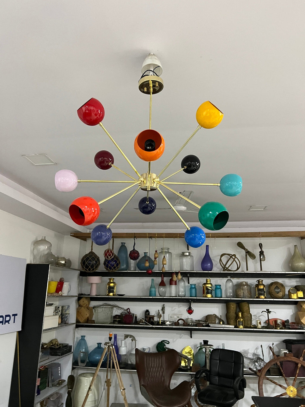Colorful chandelier hanging in a room with shelves displaying various items.