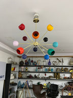 Colorful chandelier hanging in a room with shelves displaying various items.