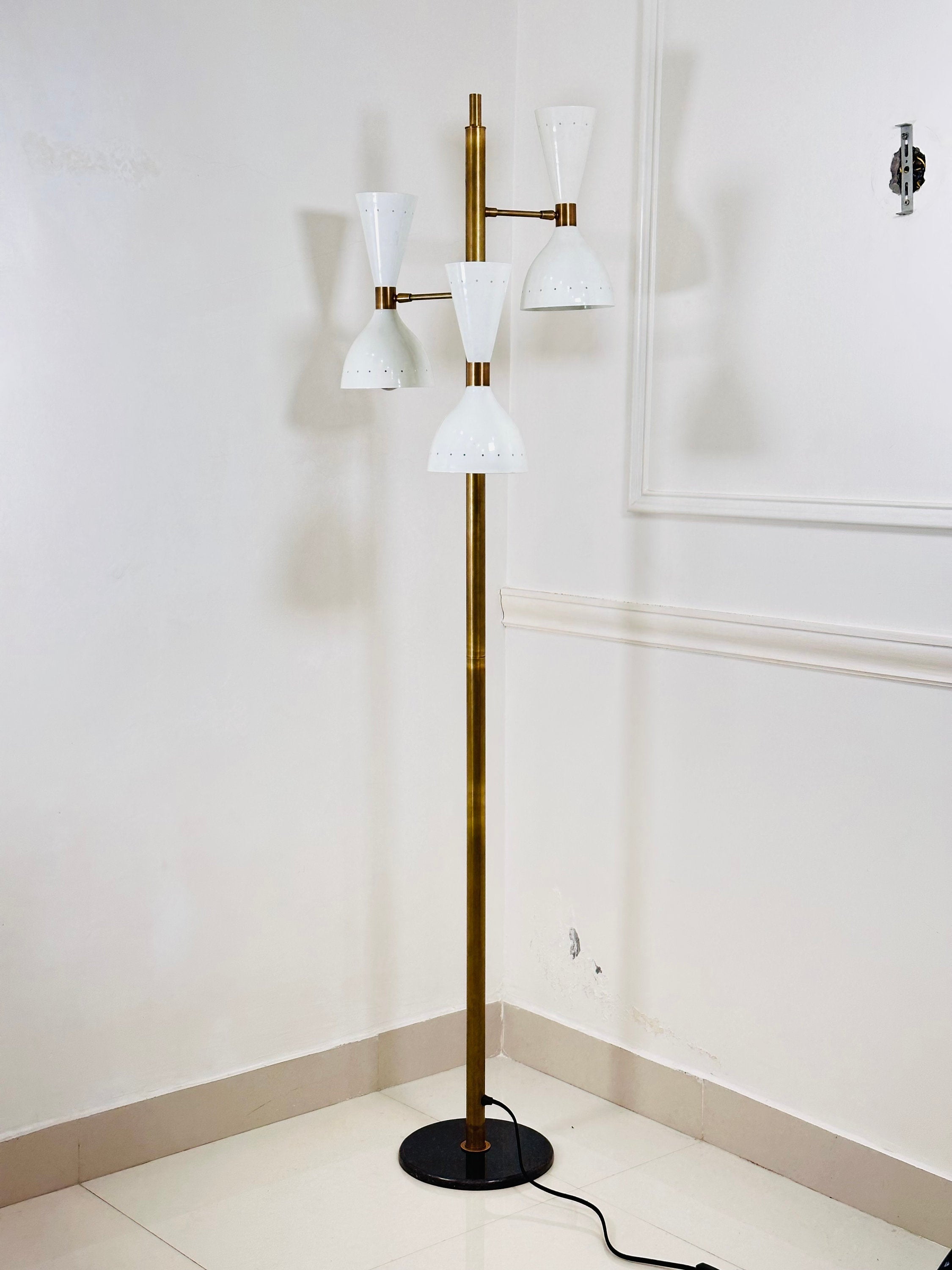 Modern floor lamp with white glass shades and gold metal base against a white wall.
