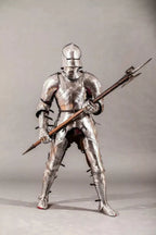 Full-body view of a person in medieval armor holding a spear on a gray background
