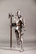 Person wearing full medieval armor holding a spear on a plain background