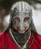 Person wearing a detailed silver helmet with intricate designs, set against a blurred natural background.