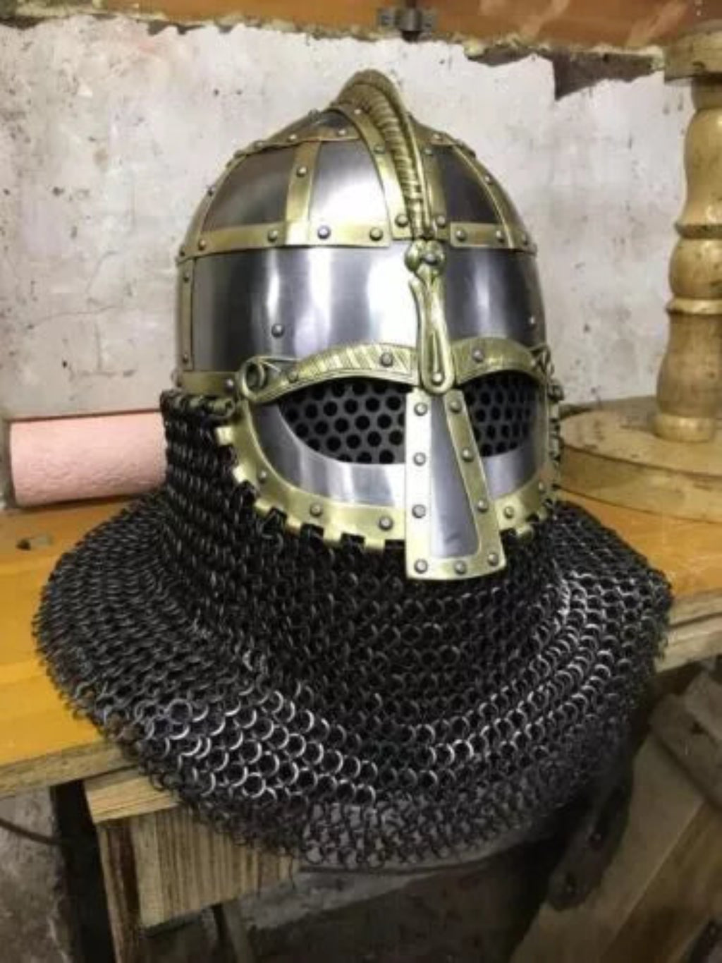 Medieval chainmail helmet with decorative elements on a wooden surface.