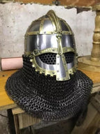 Medieval chainmail helmet with decorative elements on a wooden surface.